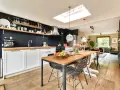 Cuisine moderne avec îlot central, parfait pour rénover vieille cuisine. Table en bois, chaises design, et mur noir avec étagères.