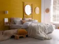 Une chambre d'adulte lumineuse avec un mur jaune soleil, un lit douillet et une décoration murale en rotin.