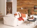 Un canapé blanc moelleux, des coussins orange et un plaid créent une deco petit salon cosy. Une porte ancienne et un mur en bois ajoutent du caractère.