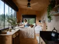 Un couple lit dans un lit douillet, profitant de l'aménagement ingénieux d'une tiny house avec vue sur la nature.