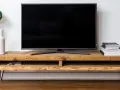 Meuble TV DIY en bois brut avec une plante verte dans un vase blanc, une pile de livres et un objet décoratif doré.