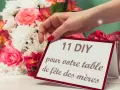 Une main dépose une carte "11 DIY pour votre table de fête des mères" près d'un bouquet de fleurs roses et blanches.