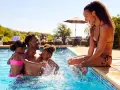 Famille s'amusant dans une piscine, un père avec ses deux filles, une mère assise au bord. Le cadre parfait pour le meilleur center parc France.