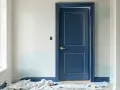 Une porte intérieure bleu marine est peinte, contrastant avec les murs clairs et les touches de bleu pâle. Le projet de peindre porte intérieure 2 couleurs est en cours.