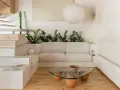Salon au style wabi sabi, avec un canapé blanc, une table basse en verre et bois, des plantes vertes et un escalier en bois brut.