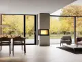 Un salon moderne avec une cheminée design, une table à manger et de grandes baies vitrées offrant une vue sur un jardin d'automne. Idéal pour moderniser une cheminée.