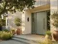 Porte d'entrée moderne couleur sauge, avec des oliviers en pot et des graminées. L'architecture épurée et la lumière douce créent une ambiance accueillante.
