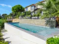 Magnifique piscine semi enterrée avec habillage en pierre, bordée par une terrasse et un jardin luxuriant, devant une villa moderne.