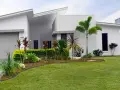 Parterre luxuriant devant une maison moderne aux lignes épurées, avec des palmiers et des plantes tropicales.