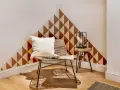 Un coin cosy avec un fauteuil en rotin, un coussin blanc et un motif géométrique sur le mur. Une belle idée motif peinture mur pour un style unique.