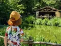 Un enfant avec un t-shirt dinosaure regarde un étang verdoyant et une étable. Le Puy du Fou, un lieu pour tous les âges.