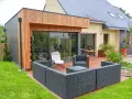 Agrandissement maison ossature bois avec terrasse moderne et mobilier extérieur.