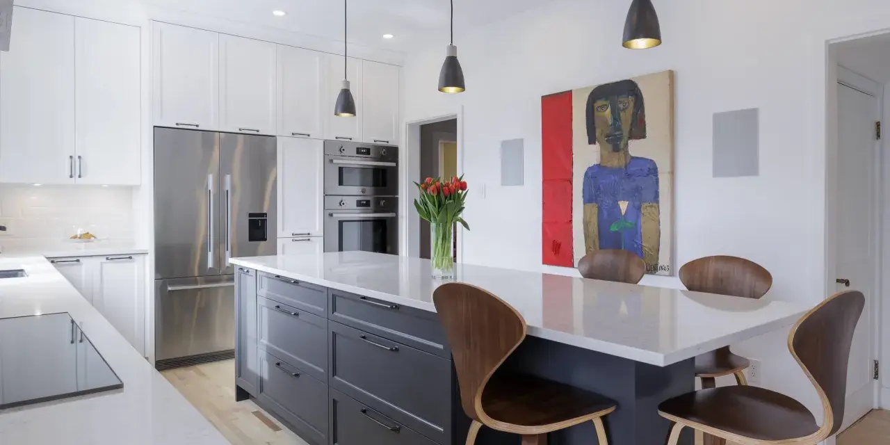 Cuisine moderne avec îlot central gris, comptoirs en quartz, armoires blanches et tableau abstrait. Idées pour comment rénover sa cuisine.
