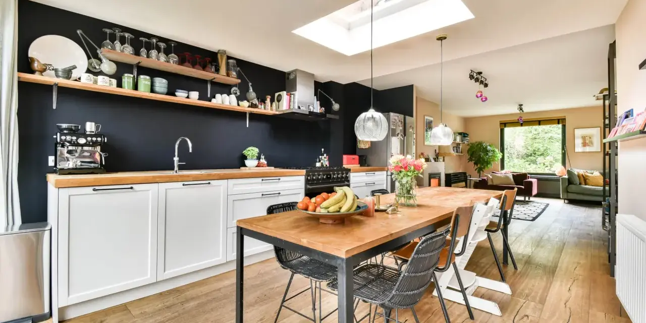 Cuisine moderne avec îlot central, parfait pour rénover vieille cuisine. Table en bois, chaises design, et mur noir avec étagères.