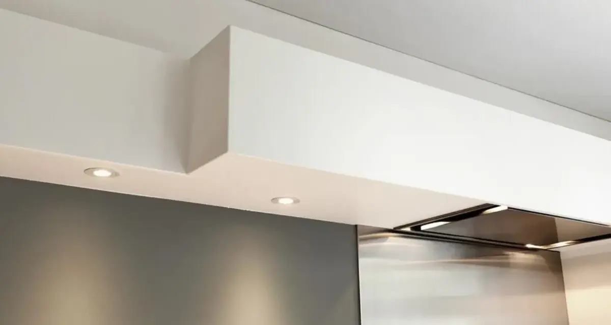 Éclairage discret sous un faux plafond de cuisine moderne, intégrant une hotte aspirante en inox.
