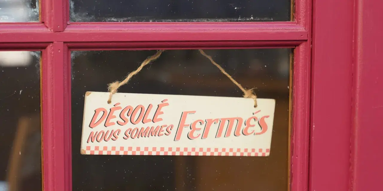 Panneau "Désolé, nous sommes fermés" sur une porte rouge. Il est donc probable que ce commerce ne soit pas ouvert le 1er mai.