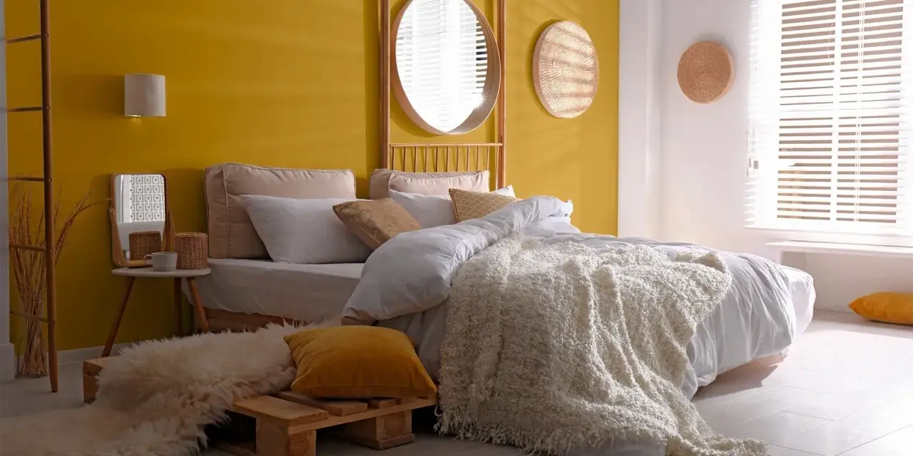 Une chambre d'adulte lumineuse avec un mur jaune soleil, un lit douillet et une décoration murale en rotin.