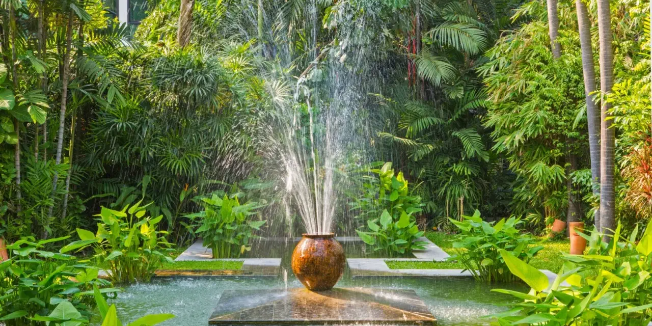 Fontaine d'eau jaillissant d'un pot en terre cuite, au cœur d'un jardin luxuriant. Une **original déco jardin récupération** qui invite à la détente.