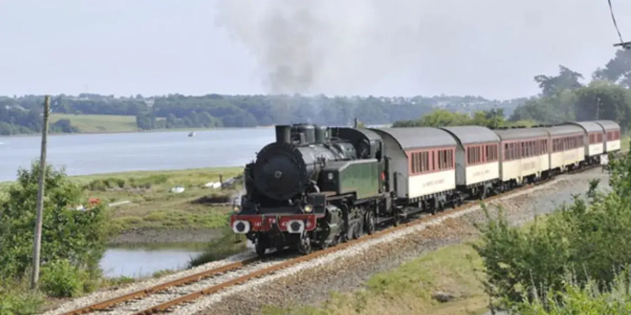 Le petit train du Trieux, avec ses tarifs attractifs, traverse un paysage verdoyant longeant une étendue d'eau.