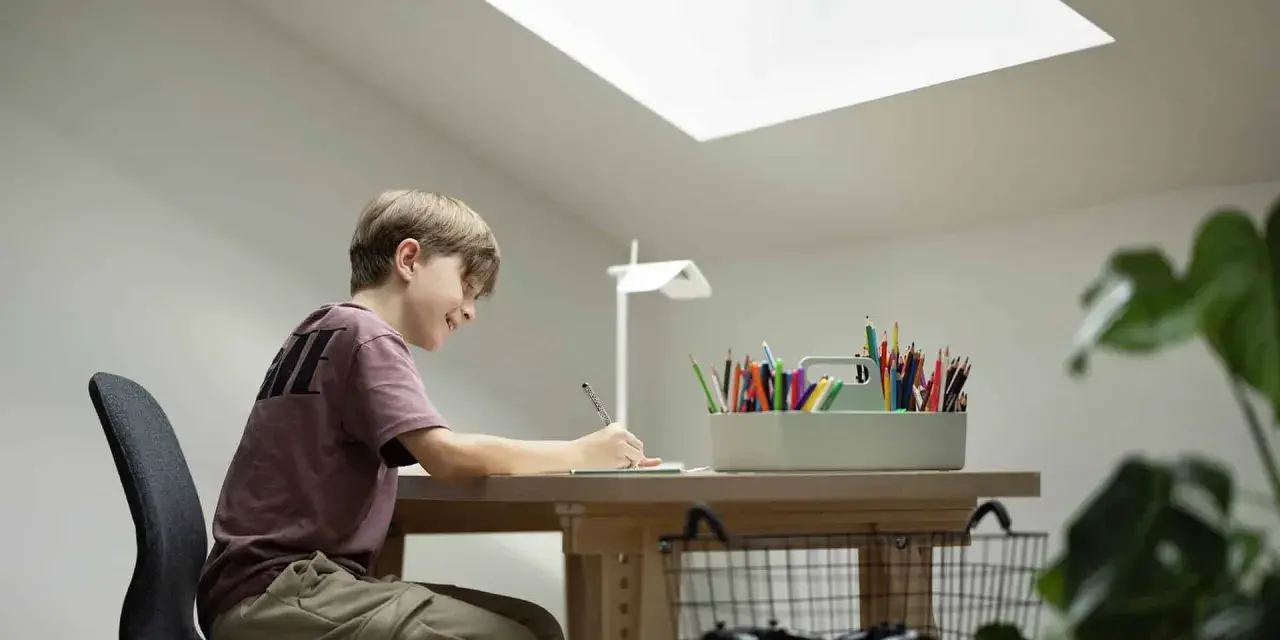 Un jeune garçon dessine joyeusement à son bureau sous pente, éclairé par une grande fenêtre de toit.