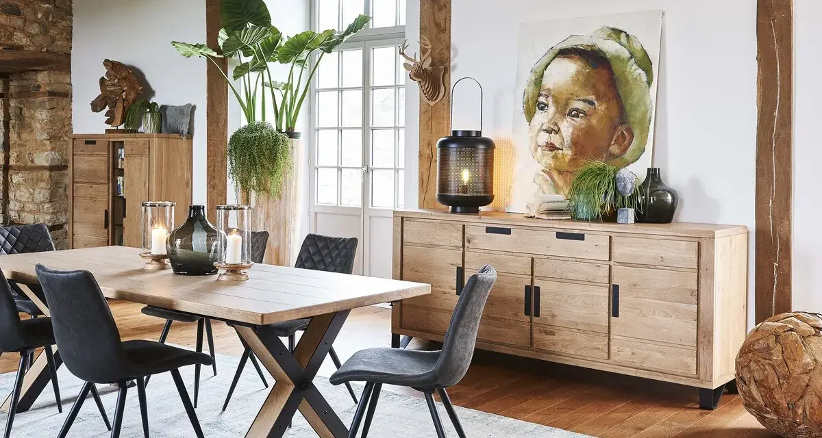 Salle à manger style industriel avec table en bois, chaises grises, buffet en chêne et tableau d'enfant.