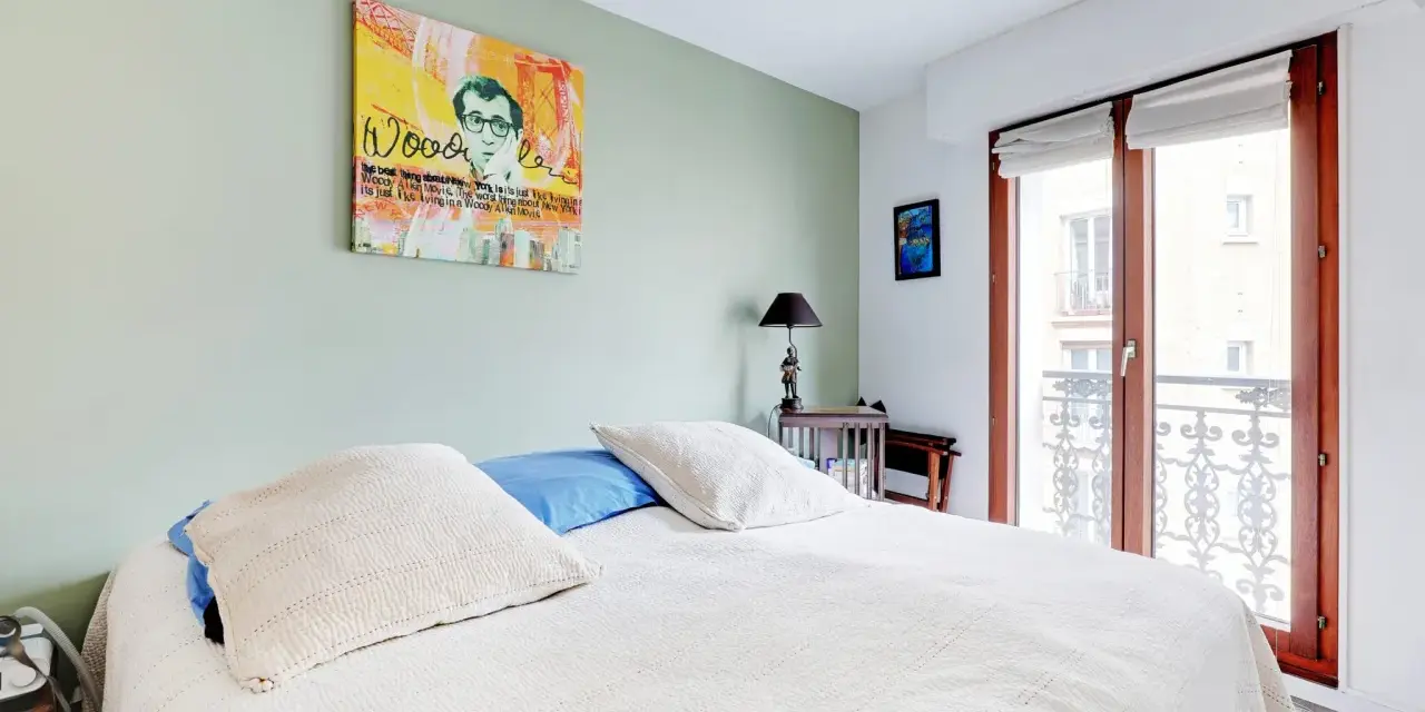 Chambre avec un mur vert pastel, un lit blanc et une œuvre d'art de Woody Allen. On dirait qu'ils ont décidé de peindre 2 murs sur 4.