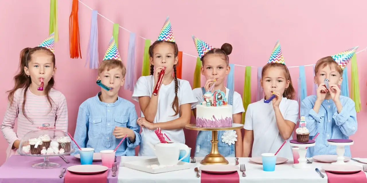 Six enfants joyeux célèbrent un anniversaire 11 ans, portant des chapeaux de fête et soufflant dans des cotillons devant un gâteau décoré.