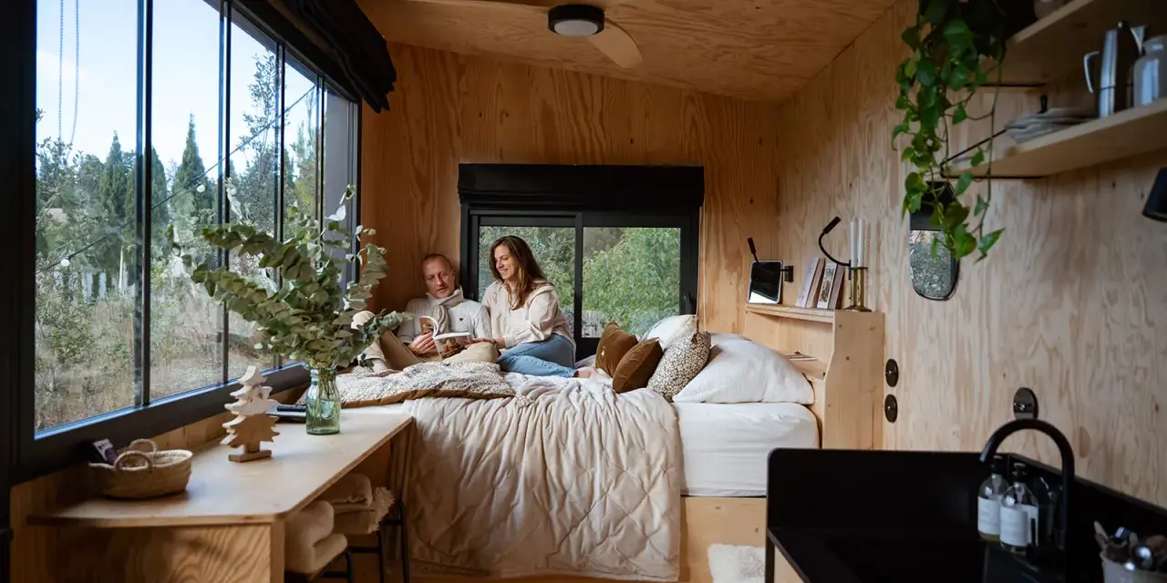 Un couple lit dans un lit douillet, profitant de l'aménagement ingénieux d'une tiny house avec vue sur la nature.
