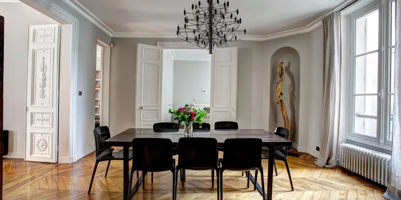 Salle à manger élégante dans un type de maison haussmannien, avec parquet ancien, lustre moderne et bouquet de fleurs.