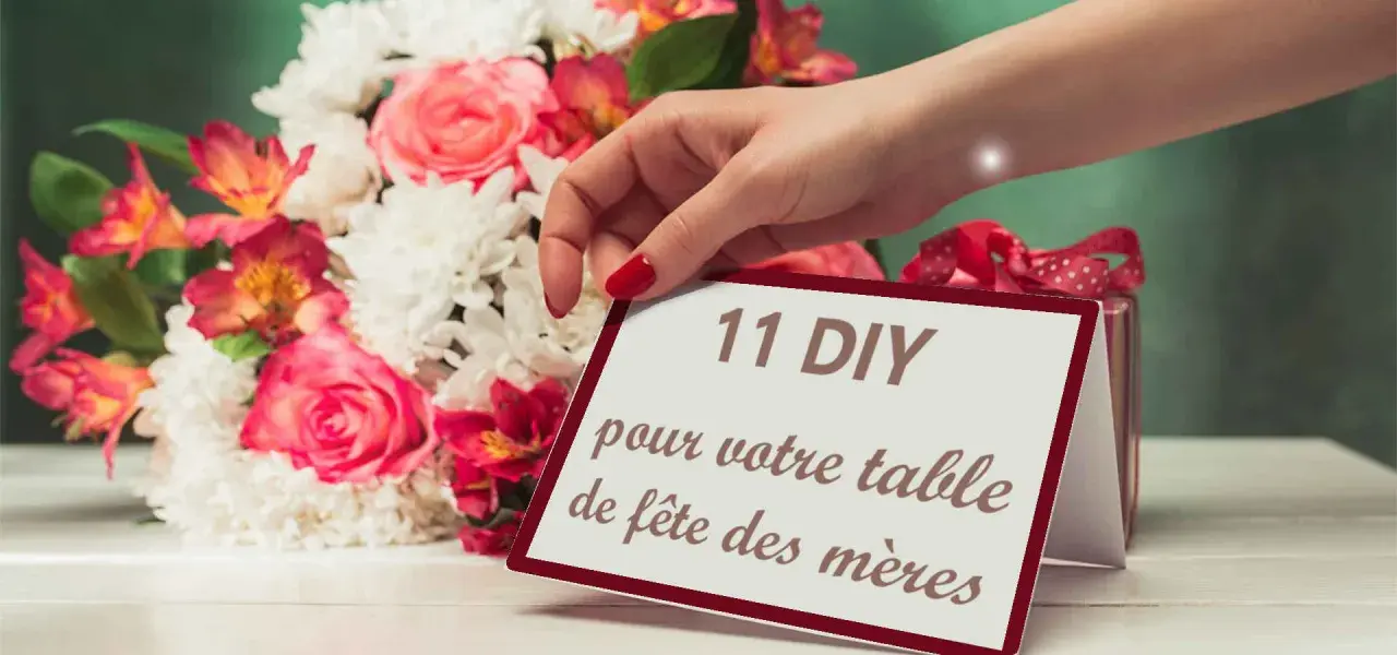 Une main dépose une carte "11 DIY pour votre table de fête des mères" près d'un bouquet de fleurs roses et blanches.