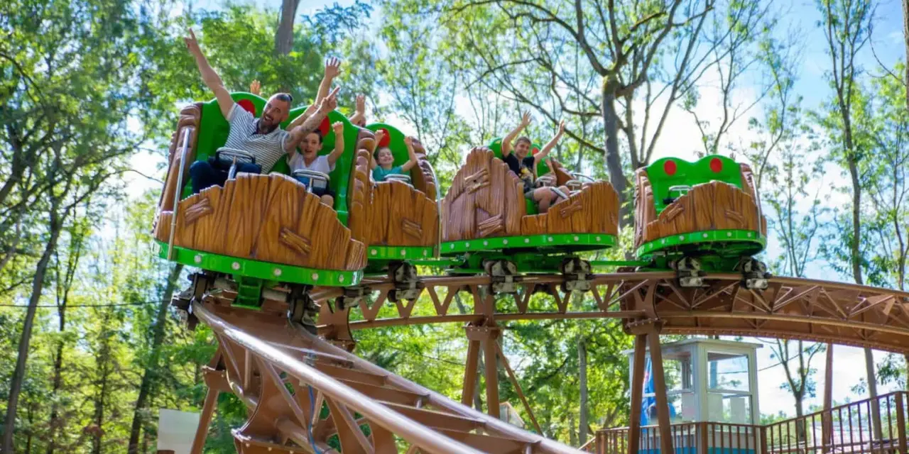 Famille joyeuse sur des wagons de montagnes russes en bois dans un parc attraction ile de france.