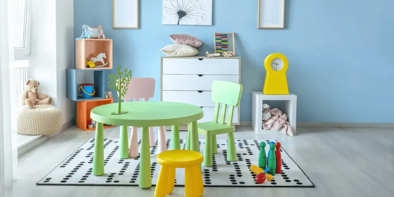 Salle de jeux lumineuse avec table verte, chaises colorées, jouets et peluche sur fond bleu clair.