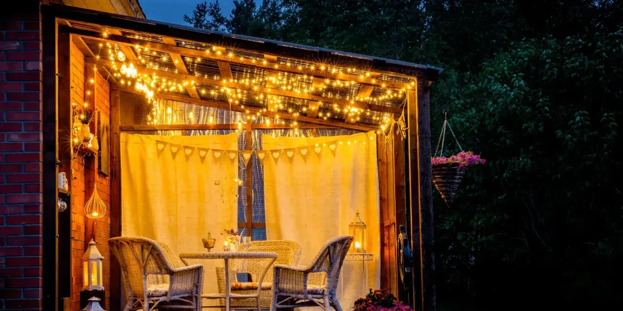 Une terrasse accueillante illuminée par des guirlandes lumineuses, une belle idée éclairage terrasse pour des soirées magiques. Meubles en rotin et fleurs ajoutent à l'ambiance.