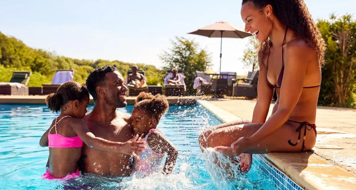 Famille s'amusant dans une piscine, un père avec ses deux filles, une mère assise au bord. Le cadre parfait pour le meilleur center parc France.