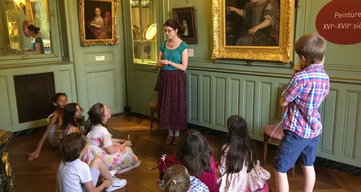 Visite guidée d'un musée dans les Yvelines : des enfants écoutent attentivement une guide devant des tableaux.