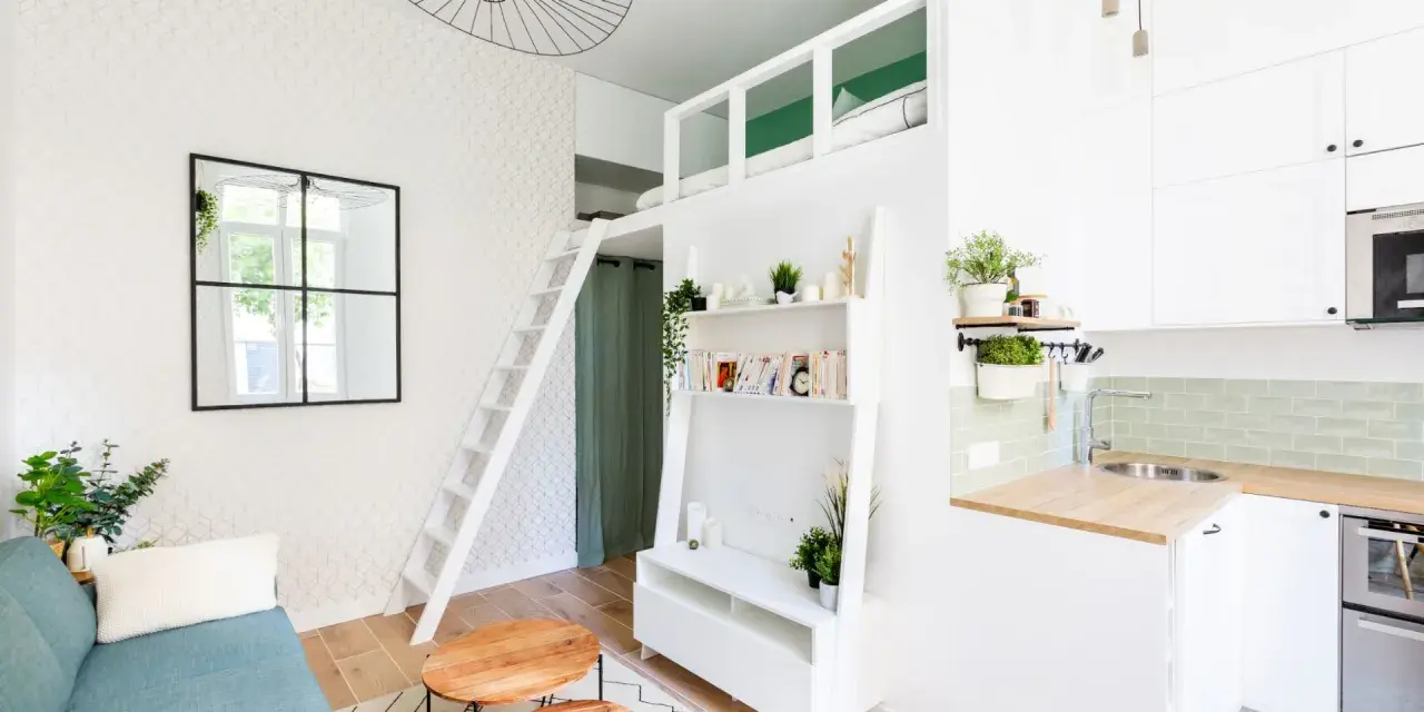 Aménagement intérieur appartement optimisé avec mezzanine, canapé bleu, étagères et coin cuisine moderne.
