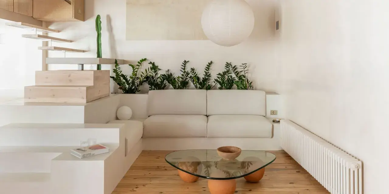 Salon au style wabi sabi, avec un canapé blanc, une table basse en verre et bois, des plantes vertes et un escalier en bois brut.
