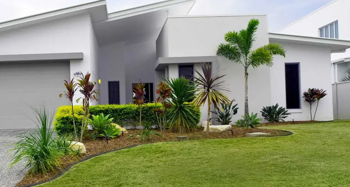 Parterre luxuriant devant une maison moderne aux lignes épurées, avec des palmiers et des plantes tropicales.