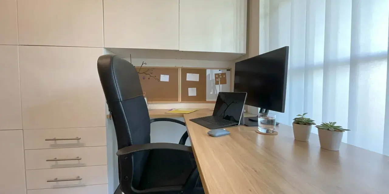 Bureau moderne avec fauteuil noir, bureau en bois clair, ordinateur portable, écran, plantes et stores blancs. Une belle idee deco bureau pour un espace fonctionnel et apaisant.
