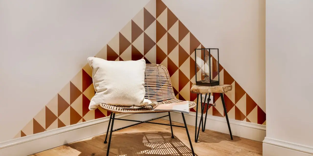 Un coin cosy avec un fauteuil en rotin, un coussin blanc et un motif géométrique sur le mur. Une belle idée motif peinture mur pour un style unique.