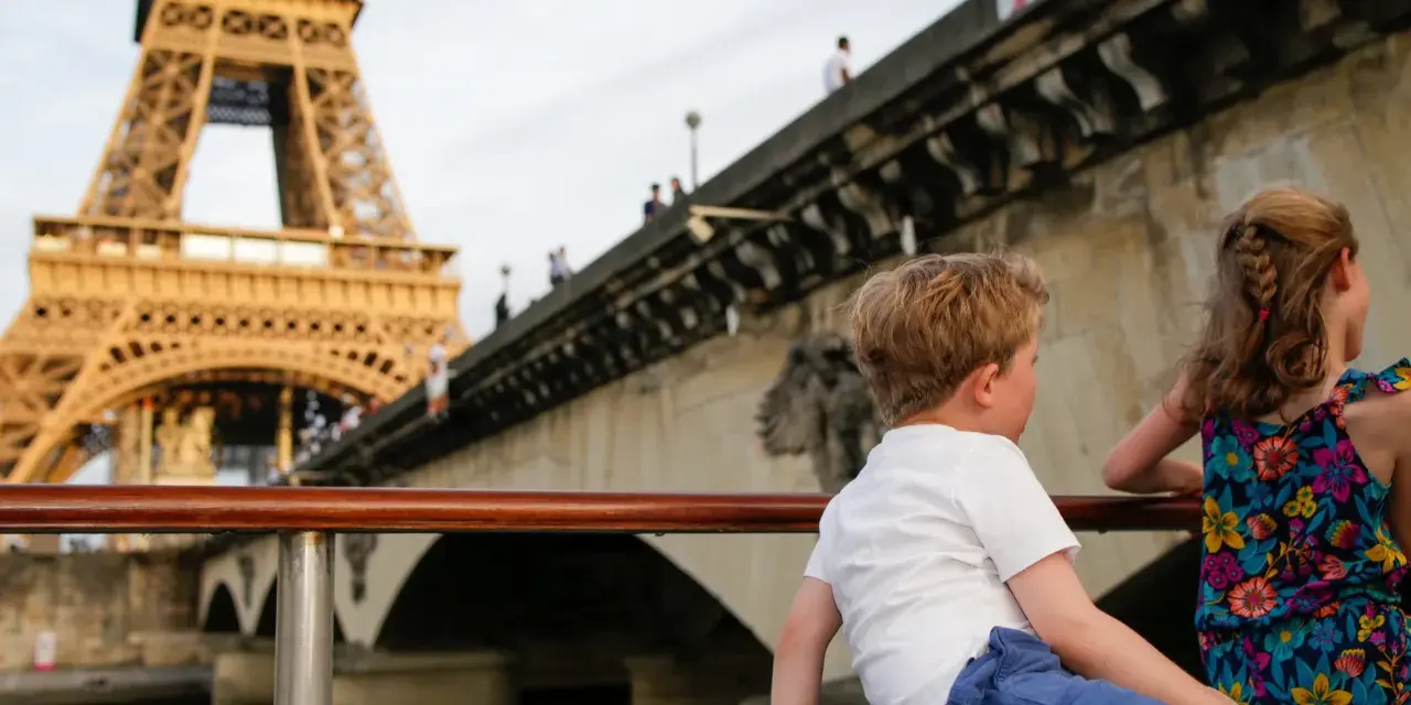 Deux enfants profitent d'une croisière sur la Seine à Paris la nuit, avec la Tour Eiffel illuminée en arrière-plan.
