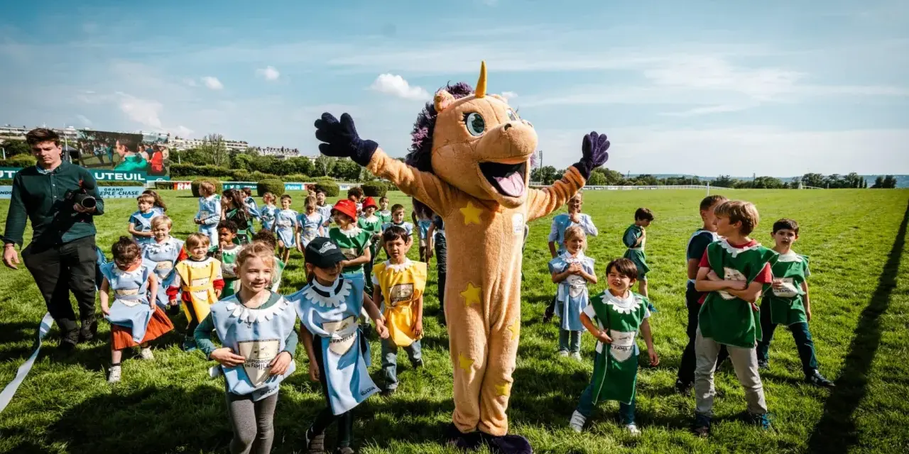 Un costume de licorne géant accueille des enfants costumés pour une journée de jeux à l'hippodrome en famille.