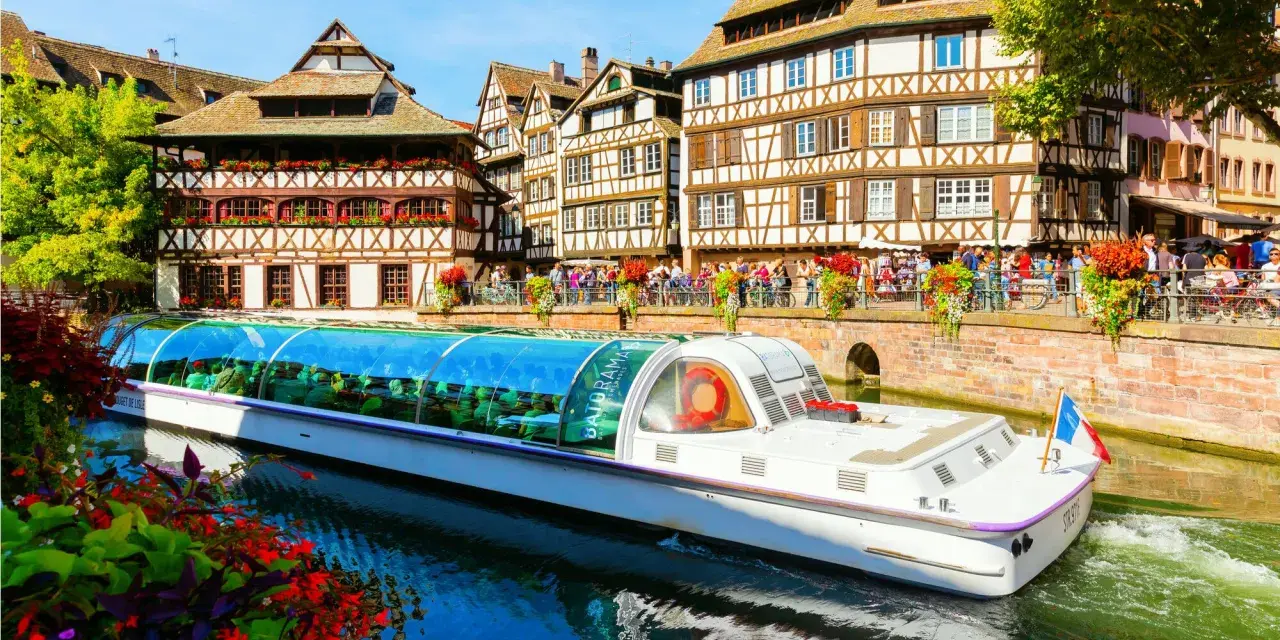 Bateau touristique naviguant sur un canal à la Petite France à Strasbourg, avec ses maisons à colombages et ses balcons fleuris.