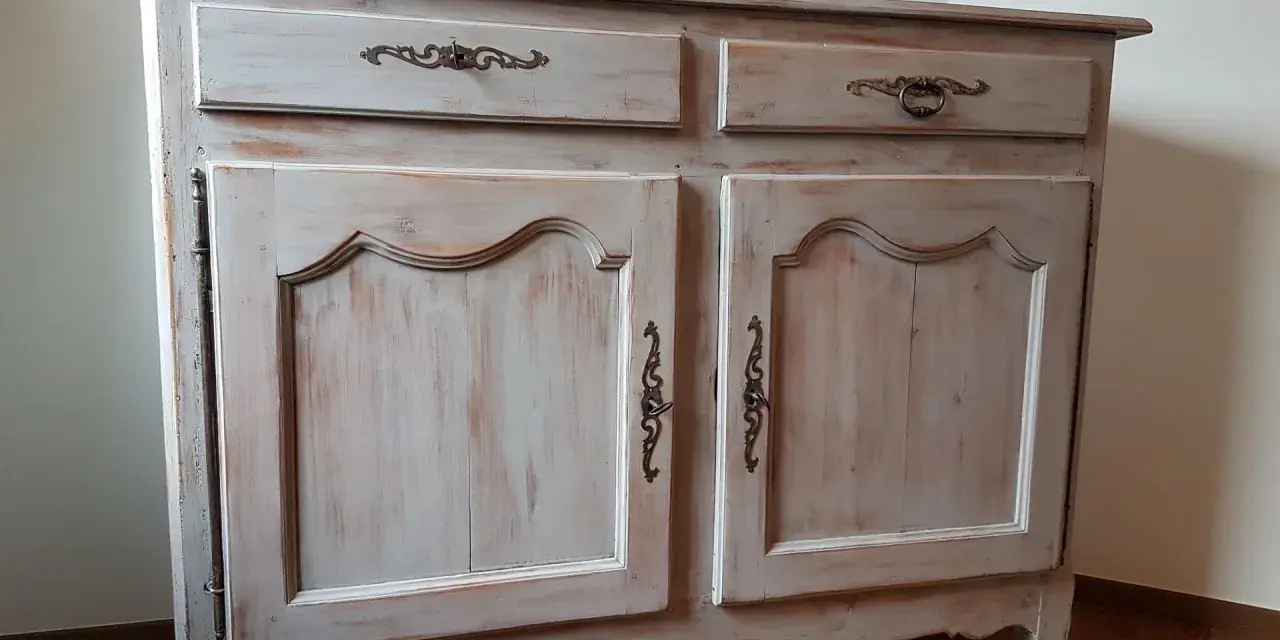 Buffet ancien patiné, avec deux tiroirs et deux portes ornées de poignées en bronze. Le bois présente une finition usée pour un style vintage.