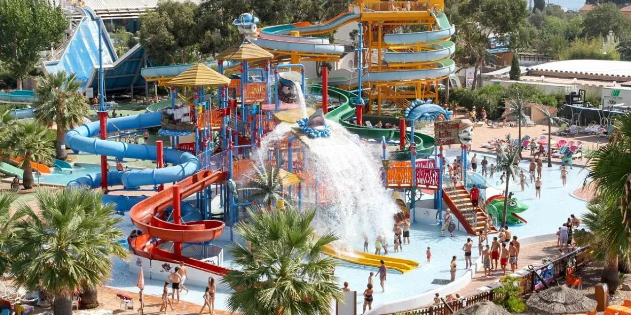 Vaste parc aquatique dans le sud de la France, avec de nombreux toboggans colorés, des jeux d'eau et des palmiers. Ambiance festive et familiale.
