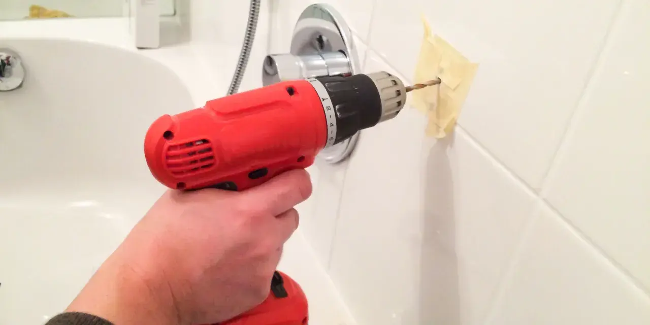 Main tenant utilise une perceuse pour percer du carrelage mural dans une salle de bain.