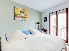Chambre avec un mur vert pastel, un lit blanc et une œuvre d'art de Woody Allen. On dirait qu'ils ont décidé de peindre 2 murs sur 4.