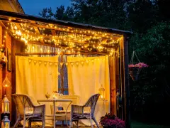 Une terrasse accueillante illuminée par des guirlandes lumineuses, une belle idée éclairage terrasse pour des soirées magiques. Meubles en rotin et fleurs ajoutent à l'ambiance.