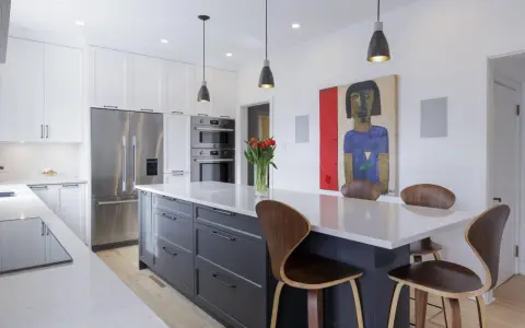 Cuisine moderne avec îlot central gris, comptoirs en quartz, armoires blanches et tableau abstrait. Idées pour comment rénover sa cuisine.