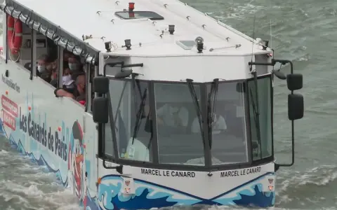 Le bus amphibie "Les Canards de Paris" navigue sur l'eau, transportant des touristes masqués pour une visite unique de la ville.